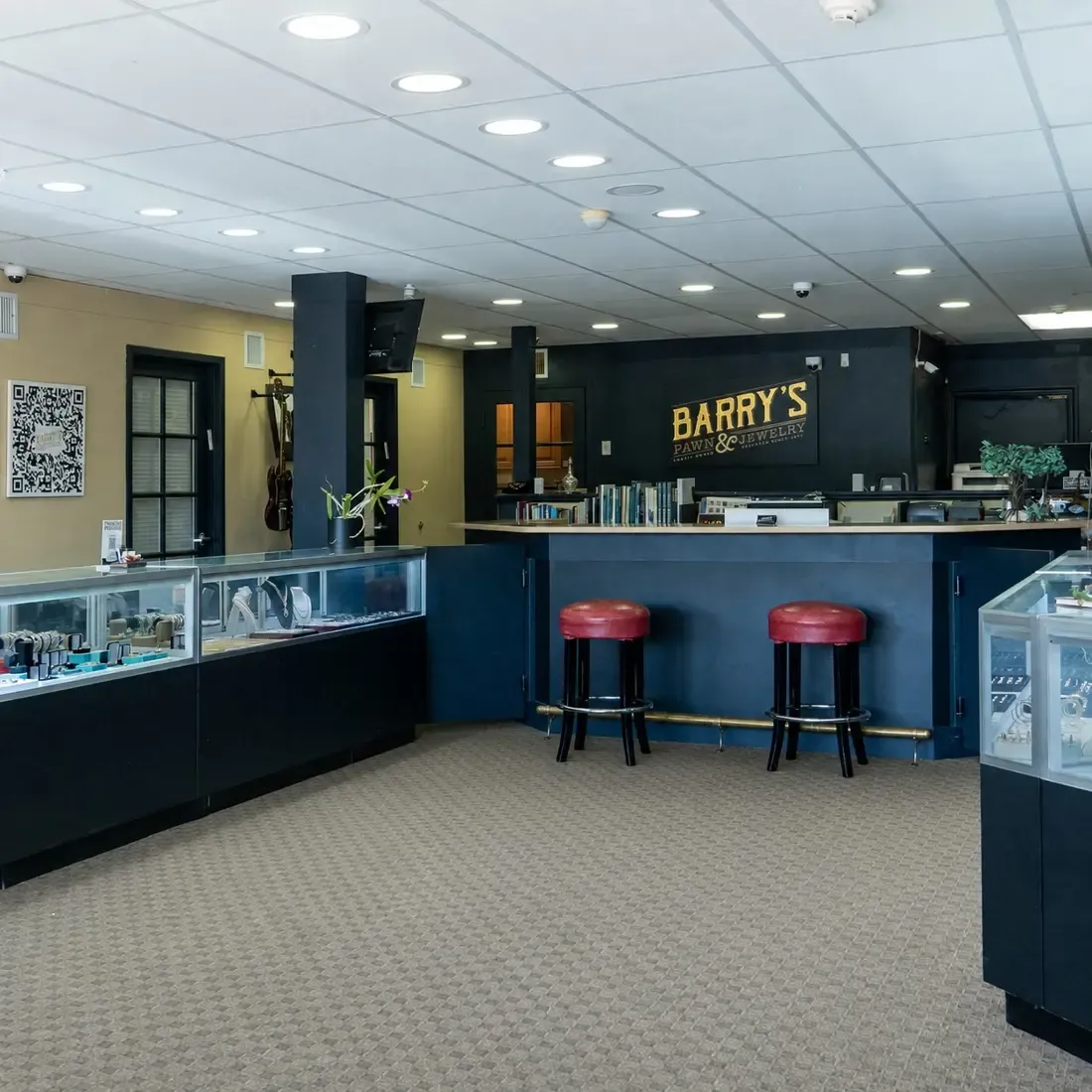Inside Barry's Pawn & Jewelry in Boca Raton: glass jewelry cases, the main counter and red stools under the Barry's sign