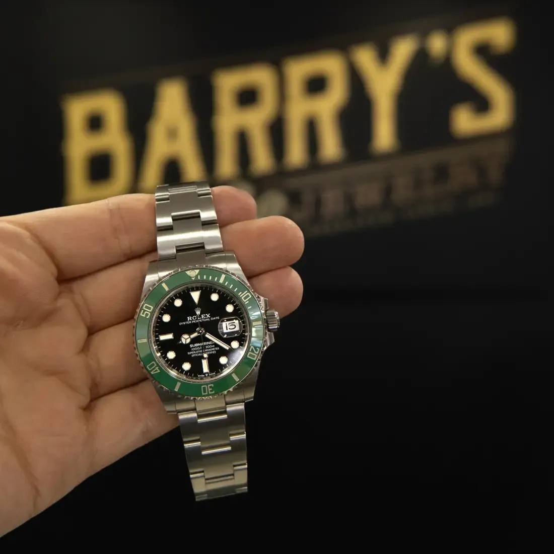 A Rolex Submariner held up in front of the Barry's Pawn & Jewelry sign inside the Boca Raton store