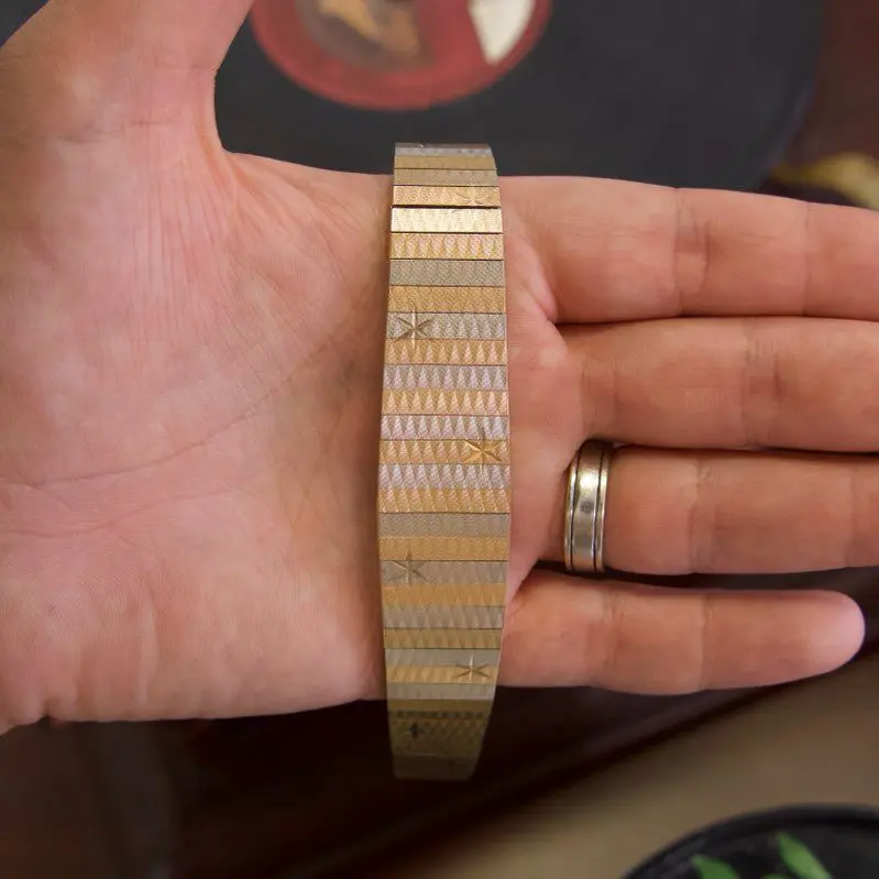 Hand holding a brass bracelet with patterns.