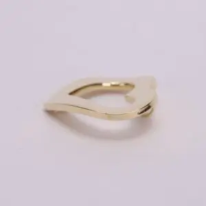 Gold, abstract-shaped metal clip on surface.