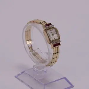 Gold wristwatch with jeweled accents on stand.