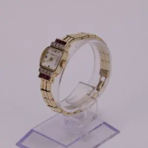 Gold watch with gemstones on stand.
