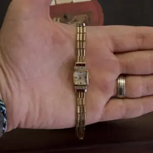 Hand holding a small vintage gold watch.