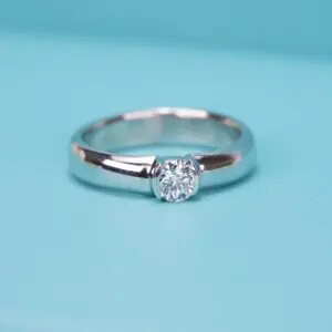 Silver ring with center diamond on turquoise background.