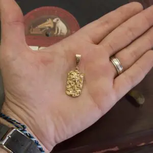Hand holding a textured gold pendant.