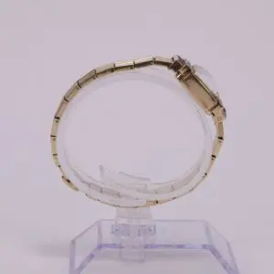 Gold wristwatch displayed on clear stand.