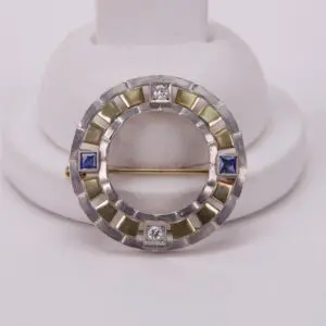 Circular brooch with blue and clear gems.