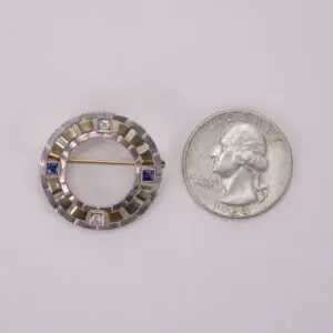 Circular brooch beside a U.S. quarter.