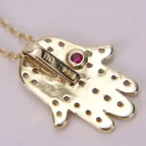 Gold pendant with red gemstone and dots.