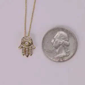Hamsa necklace beside a quarter coin.
