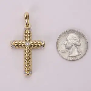 Gold cross pendant beside a quarter coin.