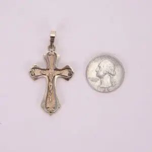 Gold cross pendant beside a silver coin.