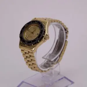 Gold wristwatch with black bezel on stand.