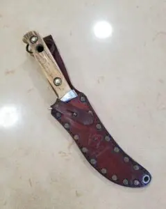 Wood-handled knife with leather sheath on table.