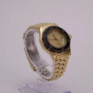 Gold wristwatch with black bezel on stand.