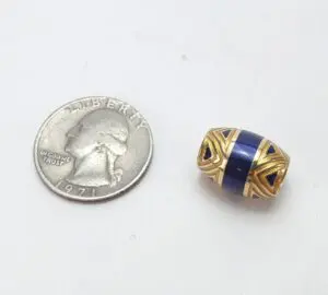 Gold and blue bead beside a quarter.