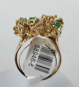 Gold ring with green gemstones and tag.