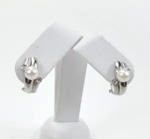 Silver earrings with pearls on display stand.