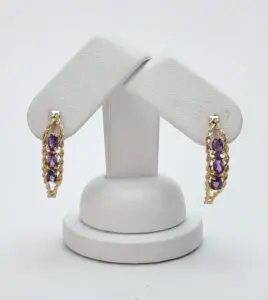 Gold earrings with purple gemstones on stand.