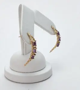 Gold earrings with purple gemstones on stand.