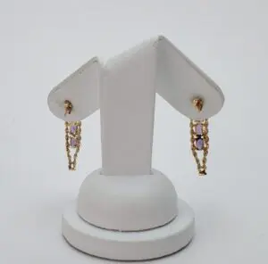 Gold earrings with purple gemstones on stand.