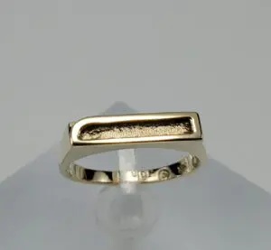 Gold ring with rectangular design on stand.