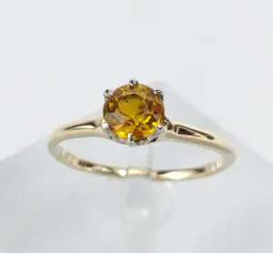 Gold ring with yellow gemstone on display.