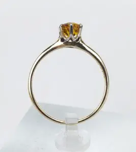 Gold ring with yellow gemstone on stand.
