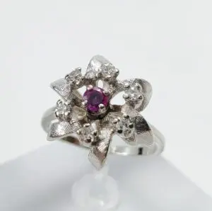 Silver flower ring with central purple gem.