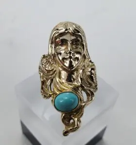 Gold ring with turquoise stone and face.