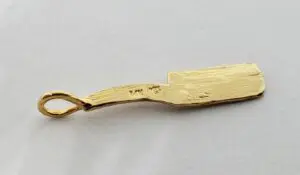Gold cricket bat-shaped pendant on white background.