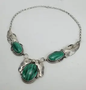 Silver necklace with green gemstones and feathers.