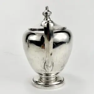 Silver teapot with ornate handle and lid.