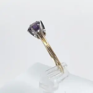 Gold ring with purple gemstone on stand.