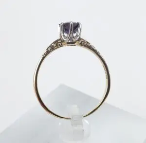 Gold ring with purple gemstone on stand.