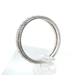 Silver ring with textured design on stand.