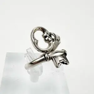 Silver ring with key design on stand.