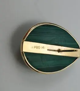 Gold brooch with green stone, engraved letters.