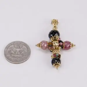 Decorative cross pendant beside a U.S. quarter.