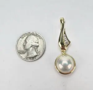 Gold pendant with pearl next to quarter.