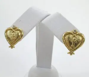 Gold heart-shaped earrings on display stand.