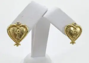 Gold heart-shaped earrings on display stand.