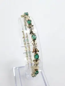 Gold bracelet with green gemstones and bows.