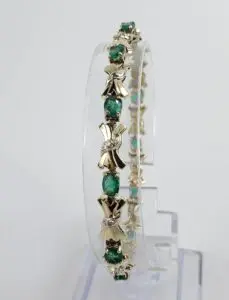 Gold bracelet with green gemstones displayed vertically.
