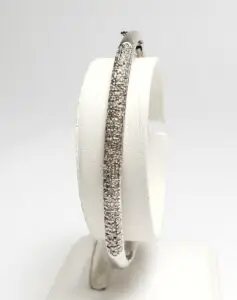 Diamond-encrusted silver bangle on display stand.