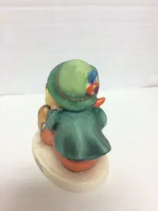Figurine of child wearing green hat and coat.