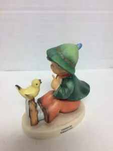 Child figurine with bird on a branch.