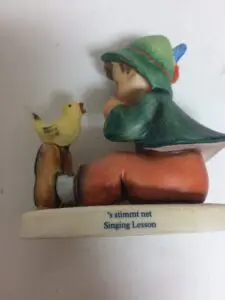 Boy figurine with bird, titled "Singing Lesson".
