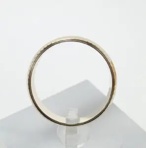 Gold ring displayed on clear stand.