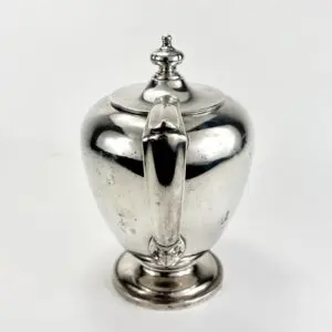 Silver teapot with ornate handle and lid.